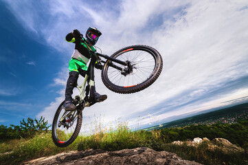 Fototapeta na wymiar professional racer jumps on a bicycle against a blue cloudy sky. Sunny summer day. Low angle view of a man on a mountain bike jumping in the mountains