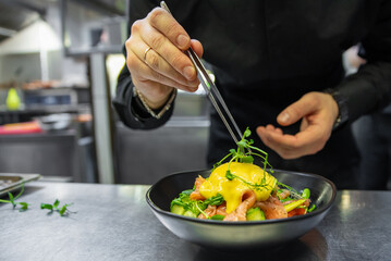 Chef in restaurant kitchen cooking salad with Boiled Eggs, Salmon, Tomatoes and cucumber in a bowl