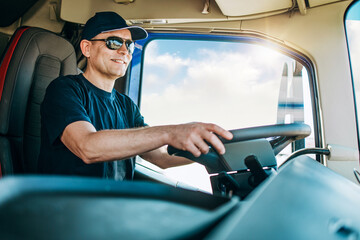 Handsome experienced male truck driver with a hat sitting and driving his truck. Professional...