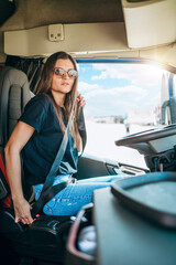 Portrait of beautiful young woman professional truck driver sitting in a big truck, looking at...