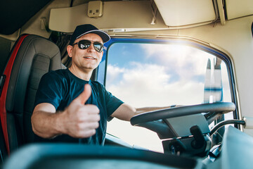 Handsome experienced male truck driver with a hat sitting and driving his truck. He is looking at...