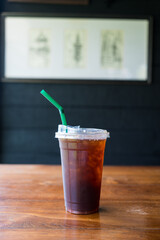Close up of take away plastic cup of iced black coffee (Americano) on wooden table.