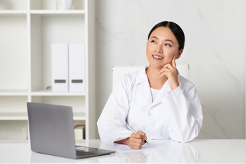 Medicine Concept. Pensive asian female doctor sitting at desk and taking notes - obrazy, fototapety, plakaty