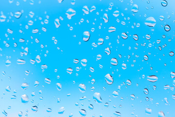 Macro shot of water droplets clinging to a glass surface . Water drops at window glass against blue sky 