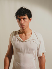Serious looking attractive young man wearing wet t-shirt, looking at camera on light background....