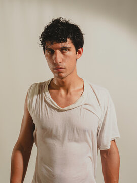 Serious looking attractive young man wearing wet t-shirt, looking at camera on light background. With green eyes and black hair