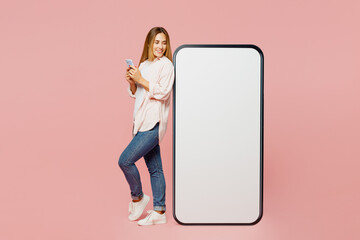 Full body side view young woman she wearing shirt white t-shirt casual clothes look at big huge blank screen mobile cell phone with area use smartphone isolated on plain pastel light pink background.