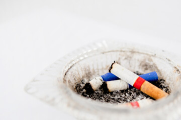 Close-up of cigarette butt in ashtray. Glass cigarette ashtray on white background. Concept of health and dangers of smoking.