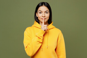 Young secret happy cool Latin woman wears yellow hoody casual clothes say hush be quiet with finger on lips shhh gesture isolated on plain pastel green background studio portrait. Lifestyle concept.