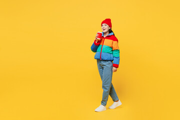 Full body young fun woman she wears padded windbreaker jacket red hat casual clothes hold takeaway delivery craft paper cup coffee to go isolated on plain yellow background studio. Lifestyle concept.