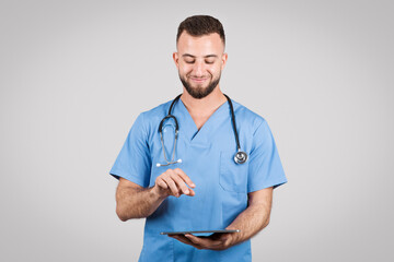 Doctor man in blue uniform using tablet and smiling on grey background