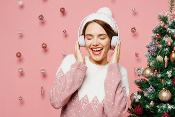Merry cheerful young woman wear white sweater hat posing listen to music in headphones have fun...