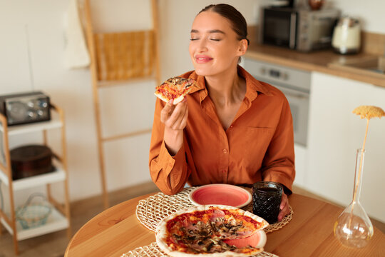 Woman savoring a slice of pizza in a cozy kitchen