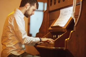 Young handsome man playing the old organ in Irish church. Indoor shot