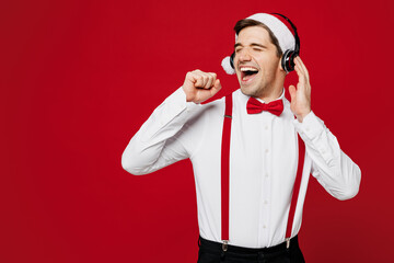 Merry young man wear white shirt Santa hat headphones posing sing song in microphone listen music...