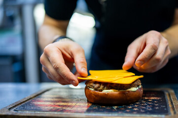 chef hand cooking cheeseburger with vegetables and meat on restaurant kitchen