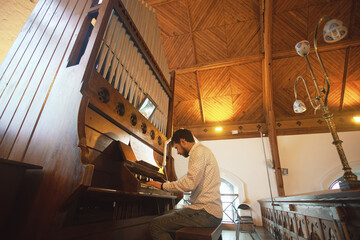 Portrait of young handsome man playing the old organ in Irish church. Perspective. Indoor shot