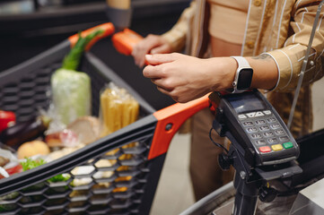 Close up cropped shot photo customer holding wireless bank terminal process acquire smart watch payment shopping at supermaket store grocery shop buy products in hypermarket. Purchasing food concept. - obrazy, fototapety, plakaty