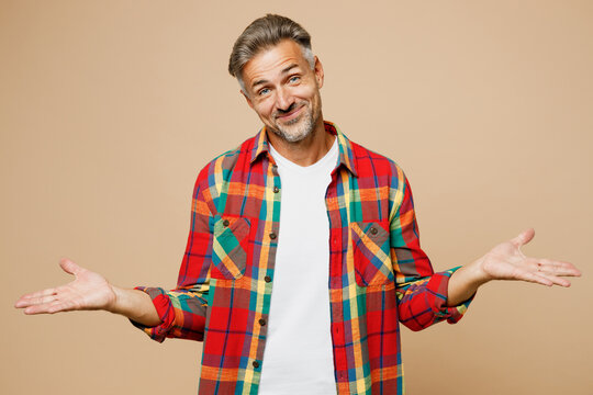 Adult sad man he wear red shirt white t-shirt casual clothes shrugging shoulders looking puzzled spread hands isolated on plain pastel light beige color background studio portrait. Lifestyle concept.