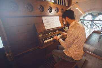 Portrait of young handsome man playing the old organ in Irish church. Perspective. Indoor shot