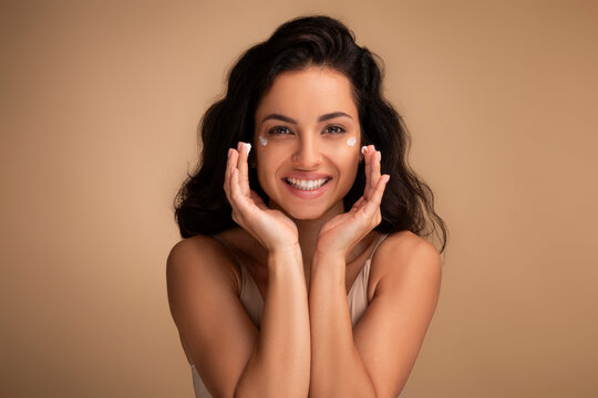 Happy beautiful indian millennial woman using moisturizing eye cream