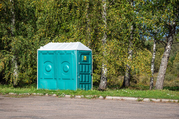 Green mobile public toilet for the disabled stands on the side of the road against a background of birch trees.