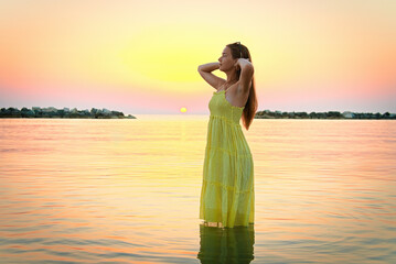 A young woman straightening her hair meets the sunrise, going into the sea