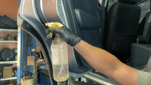 Spraying white spirit on car doors to remove rust. The master removes all the rust from the door and door card with a chemical liquid - acetone. Removal of rust from the metal surface of the car body.