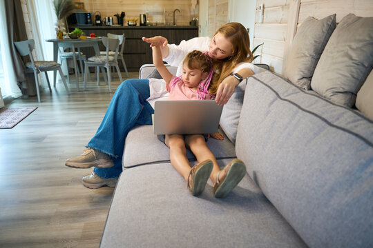 Caring mother helping her little schoolgirl doing math homework online