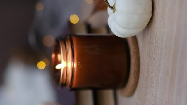 Autumn home disign: burning candle, with lights and glasses on table in cozy living room.Defocused.