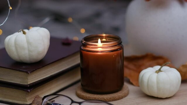 Autumn home disign: burning candle, with lights and glasses on table in cozy living room.