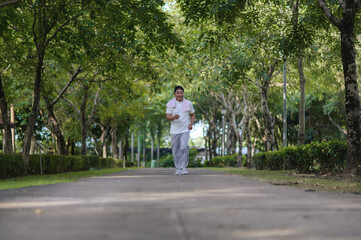 Asian Old Adult Happy Man Jogging Alone In A Park With Green Trees Background.