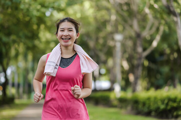 An Asian woman running in a public park surrounded by lush greenery and fresh air, She felt refreshed by the fresh air and the beautiful scenery.