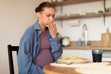 Pregnant woman feeling nausea from food smell in kitchen