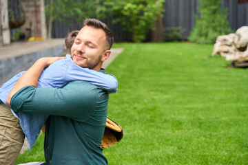 Naklejka na ściany i meble Smiling father hugs son on green lawn
