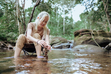 Woman sit on camping chairs to build natural stone arrangements, Balance stones in the stream with natural forest background, Trying management to find a balance. Concept of management and harmony.