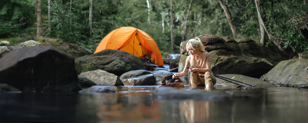 Asian woman sitting on a camping chair in the natural stream with a Camping tent in the background,...