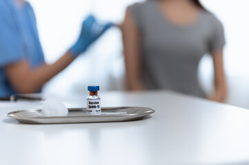Close up coronavirus covid-19 vaccine bottle on clinic table with blur nurse or medical staff inject vaccine for patient woman for prevent coronavirus infection. Health care medical vaccine concept.