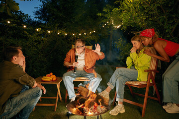 Teenager having fun at bonfire telling horror stories spending time at campsite