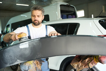 Automobile repair shop worker polishing auto body panel with buffer
