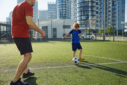 Father and son playing soccer training on football pitch during sunny summer day