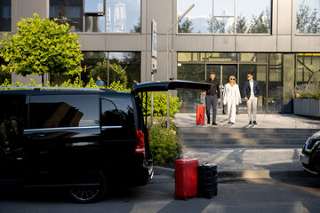 Driver or concierge helps a business couple carry their suitcases to the office or hotel from a minivan taxi. Concept of business travel and transportation service - obrazy, fototapety, plakaty