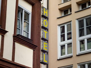 Hotel sign with vertical letters on a building exterior. The hospitality branch has accommodations in an old town. Advertisement of the tourism industry on the house facade.