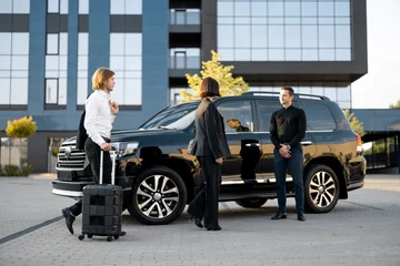 Foto op Canvas Businessman and businesswoman walk with a suitcase to a luxury black car during a business trip. Male chauffeur waiting near vehicle. Concept of transportation and business travel © rh2010