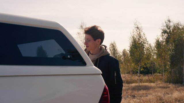 A guy opens the trunk of a car and drinks hot tea from a large metal thermos during stopover on a trip