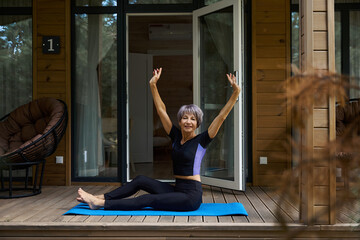 Joyful lady performs physical exercises on a wooden terrace