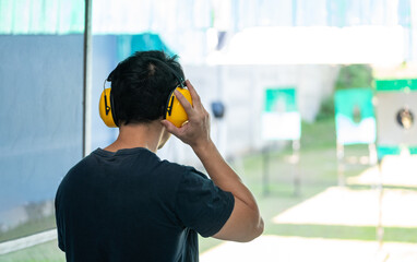 Asian shooter man wearing noise canceling headphones and black clothes practicing shooting short gun at the shooting range. Shooting sports for meditation and self-defense, recreational activities.
