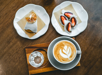 An overhead view of a cozy café table setting featuring two plates with dessertvwith a slice of cake garnished with a dried lemon slice