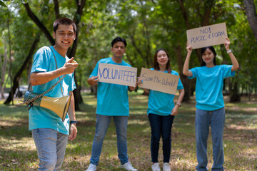 Happy young Asian students diverse volunteers hold a campaign sign for cleaning in the park, The concept of environmental conservation on world environment day, recycling, charity for sustainability.