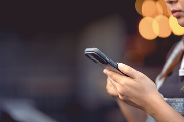 Woman's hand is using a smartphone on the side of the road and has beautiful bokeh lights.